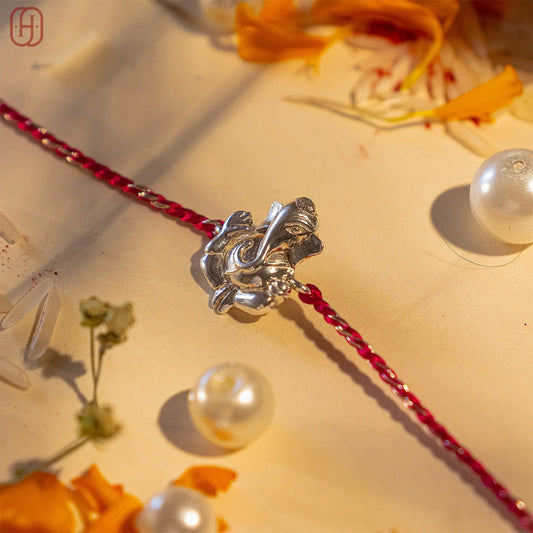 Ganesh silver rakhi with detailed Ganesh charm on a red and silver braided thread by Hardik Jewels