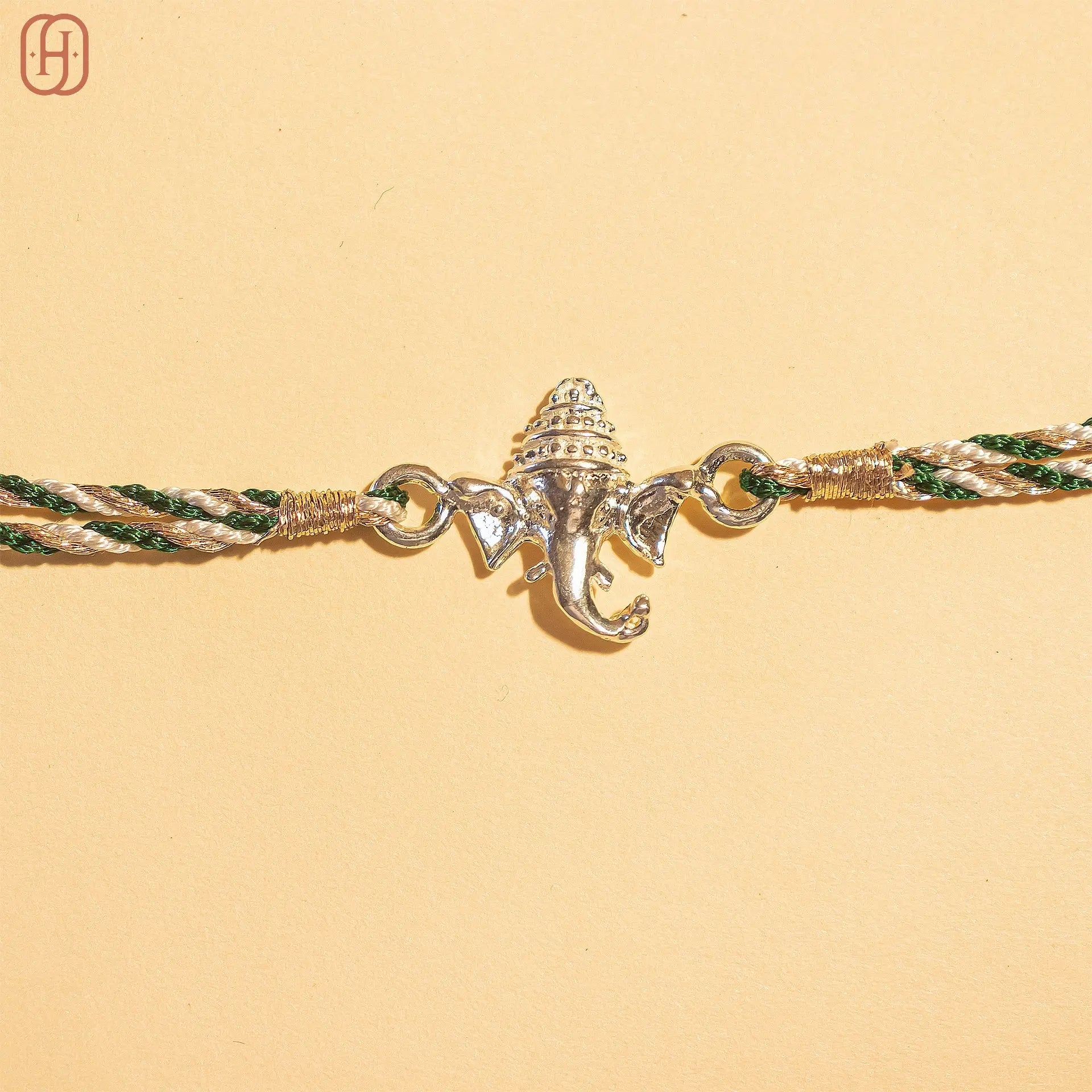 Ganesh silver rakhi with intricate elephant design and green and gold braided thread by Hardik Jewels