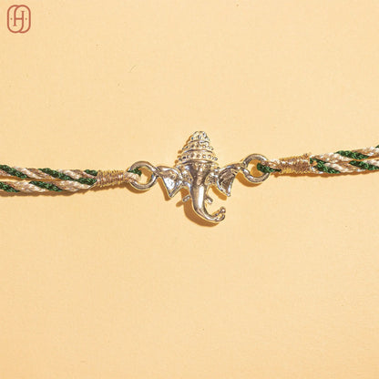 Ganesh silver rakhi with intricate elephant design and green and gold braided thread by Hardik Jewels