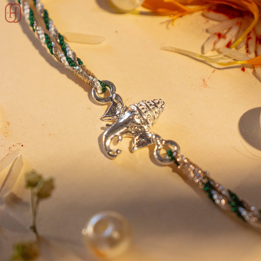 Ganesh silver rakhi with intricate elephant charm and green and silver braided thread by Hardik Jewels
