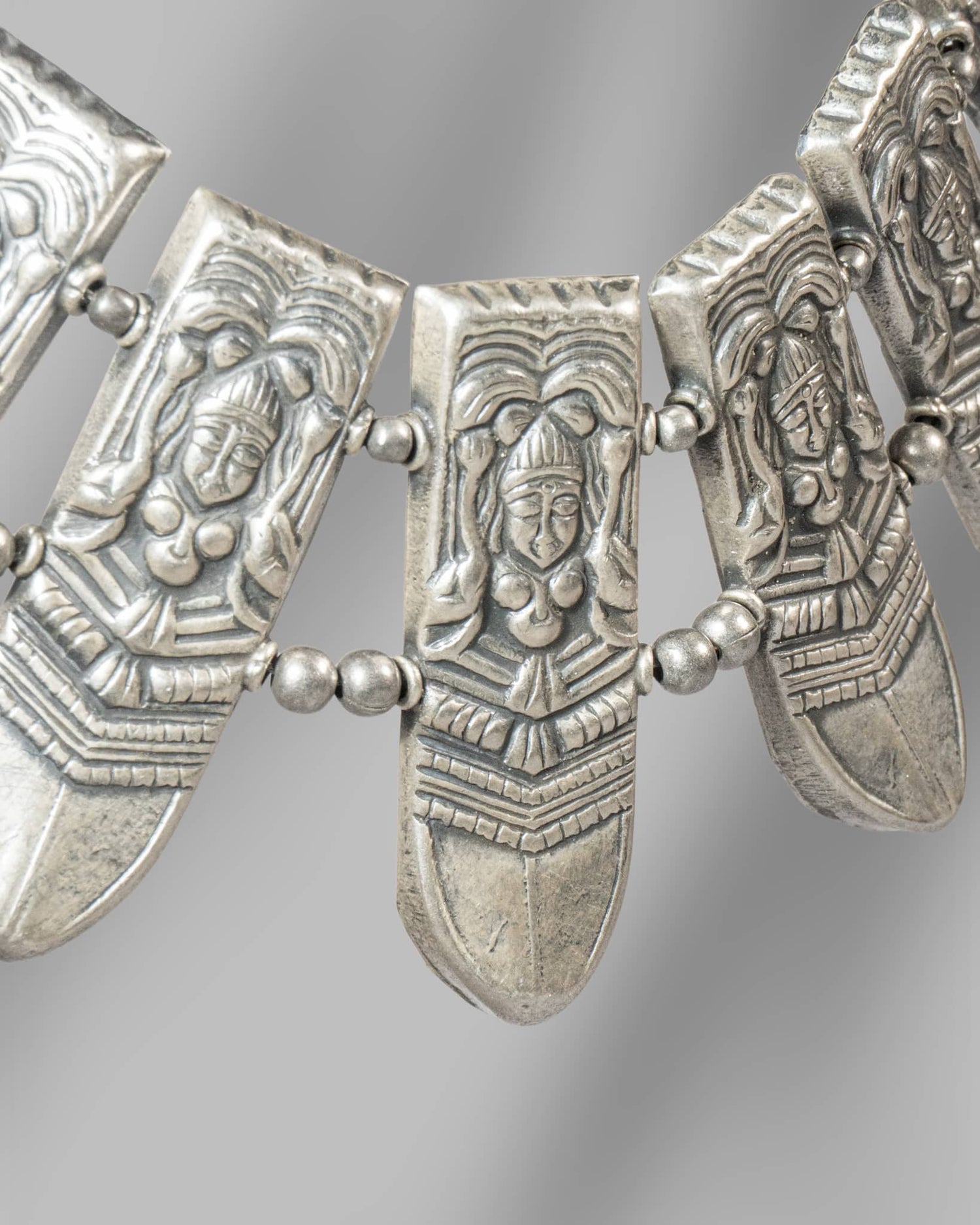 Decorative silver necklace with face-like pendants on a gray background