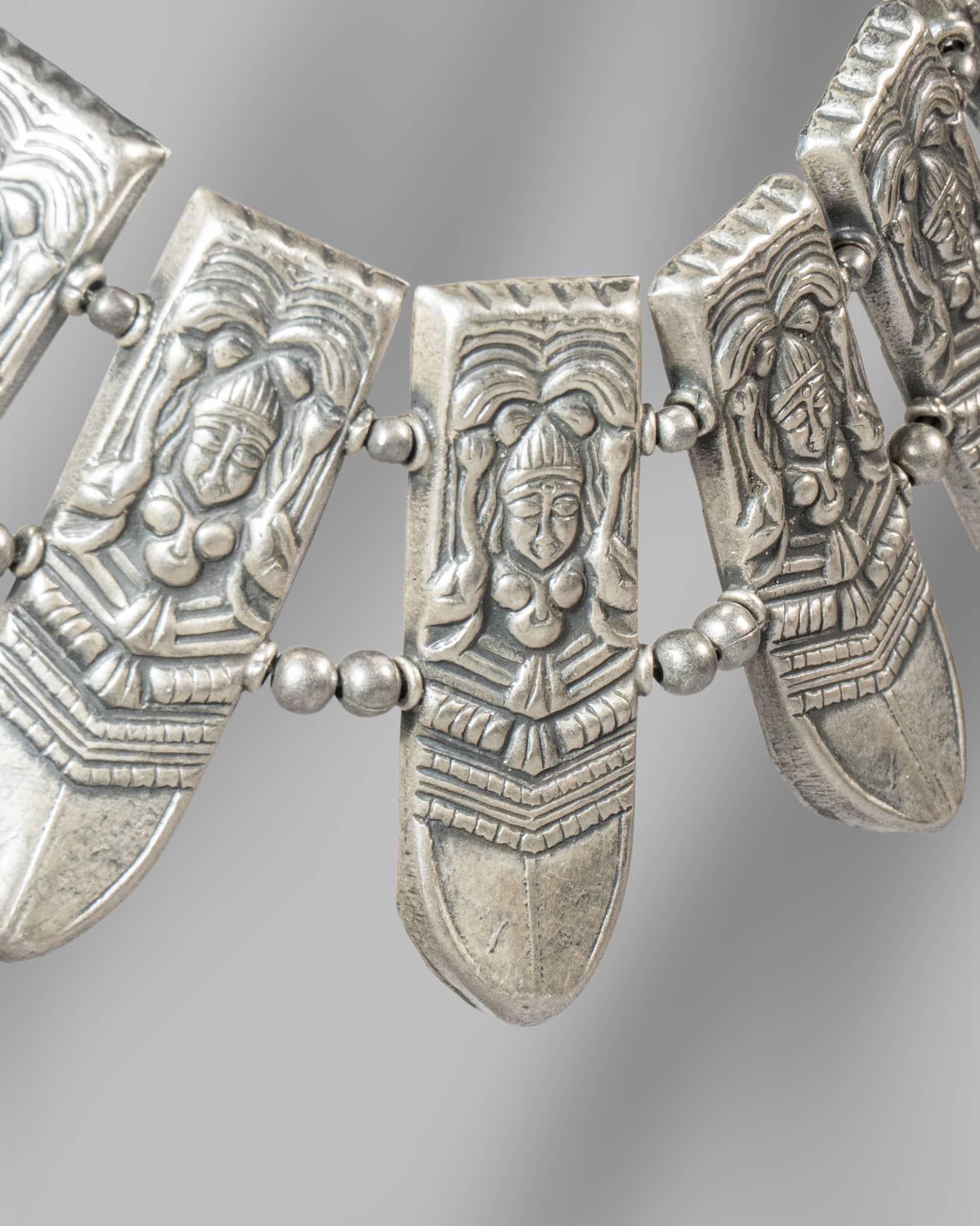 Decorative silver necklace with face-like pendants on a gray background
