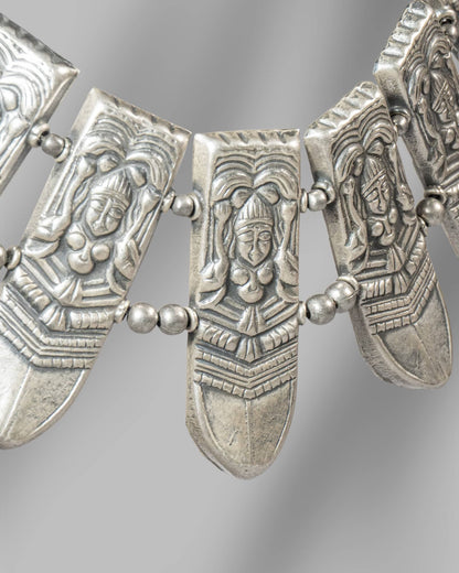 Decorative silver necklace with face-like pendants on a gray background