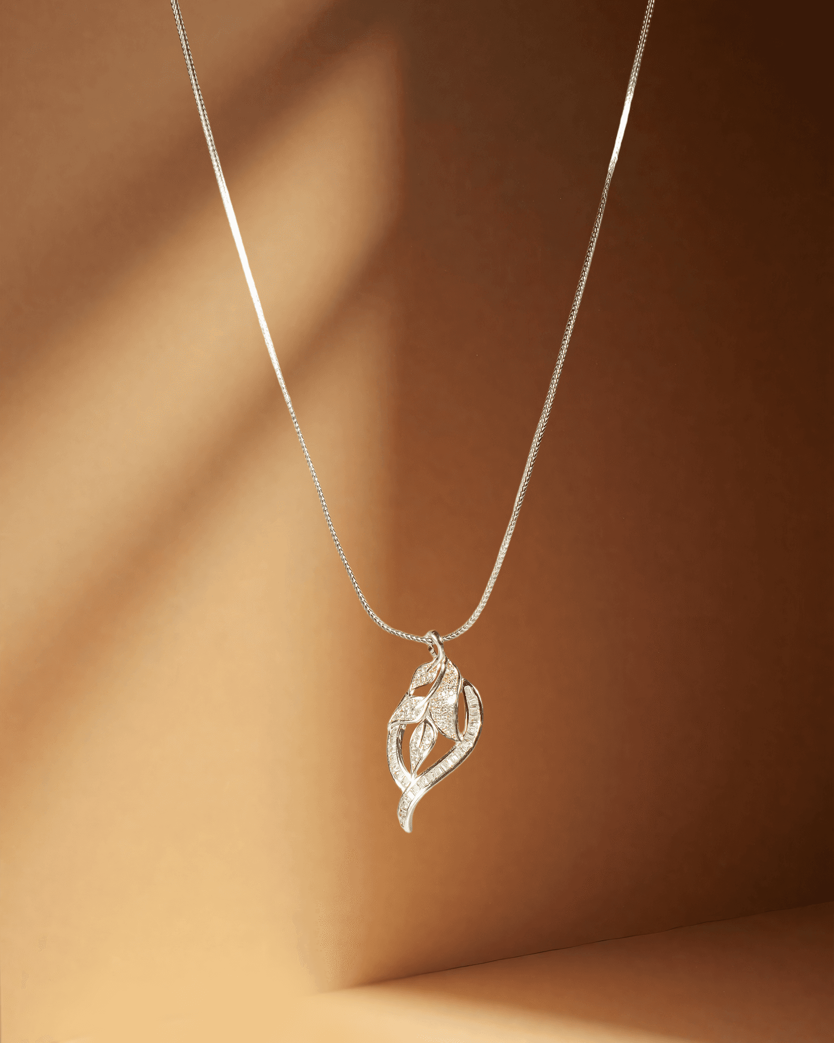 Silver pendant with a leaf-shaped pendant on a brown background