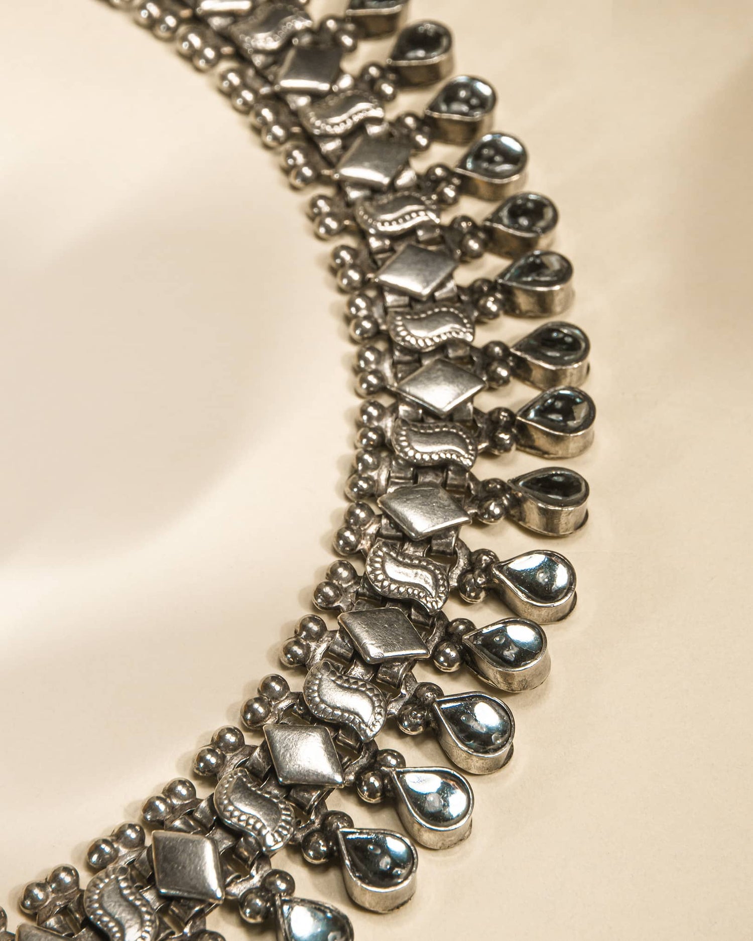 Close-up of a silver anklet with teardrop-shaped charms on a beige background