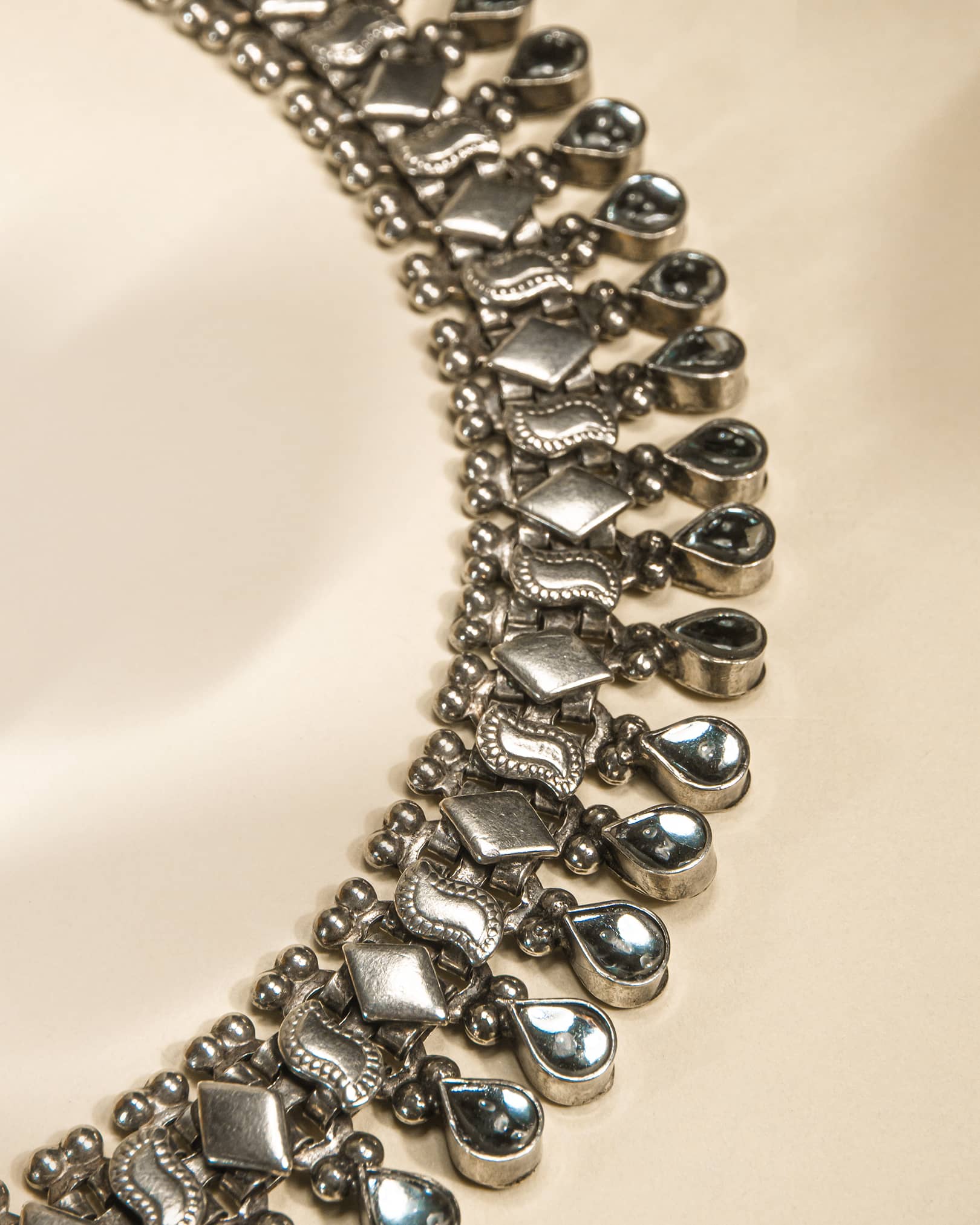 Close-up of a silver anklet with teardrop-shaped charms on a beige background