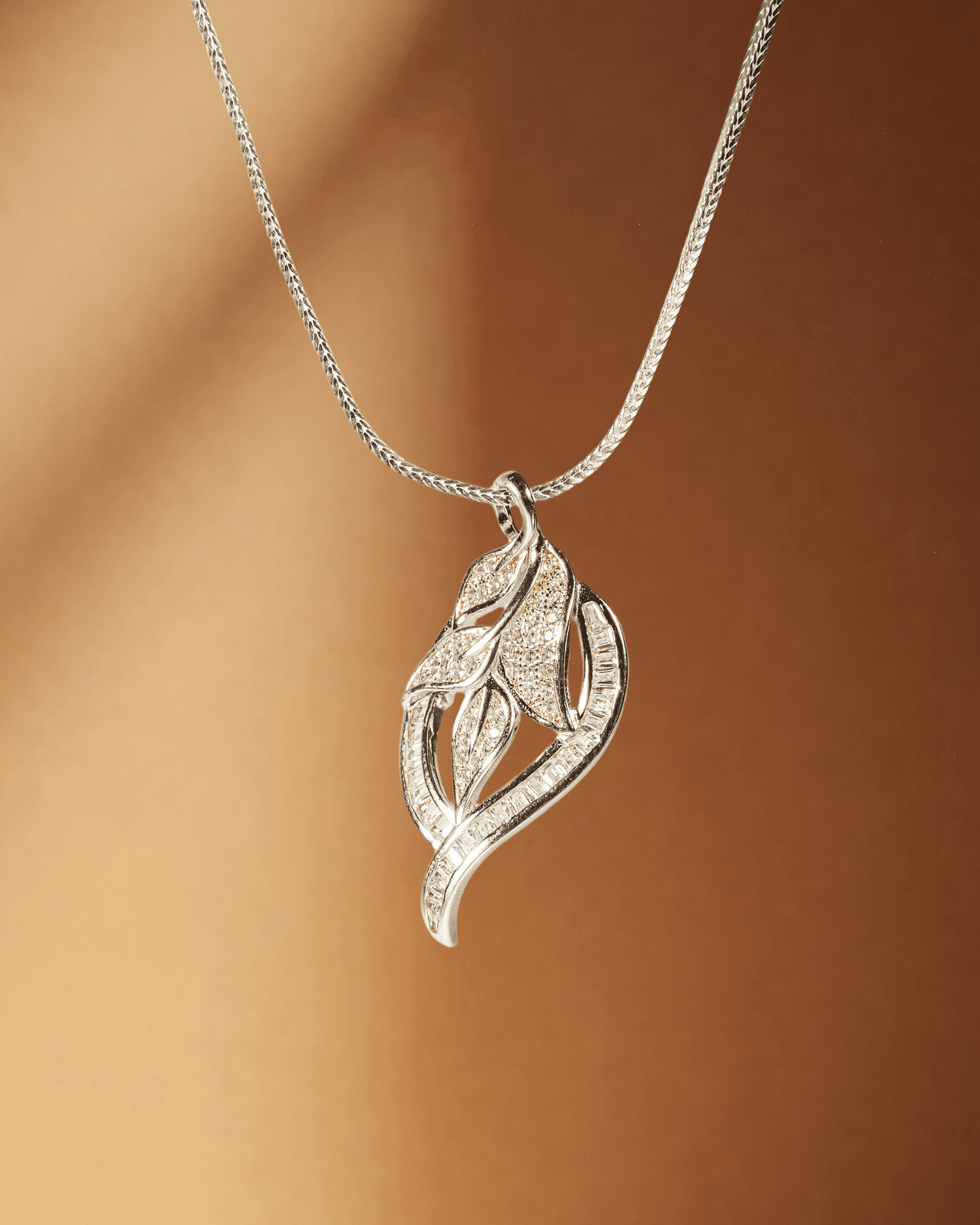 Silver leaf-shaped pendant on a chain against a brown background