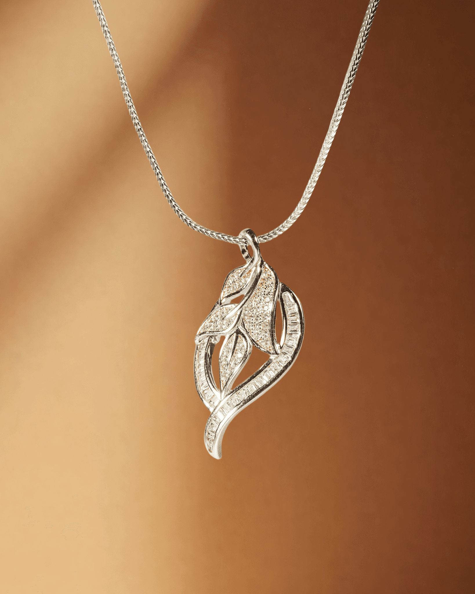Silver leaf-shaped pendant on a chain against a brown background