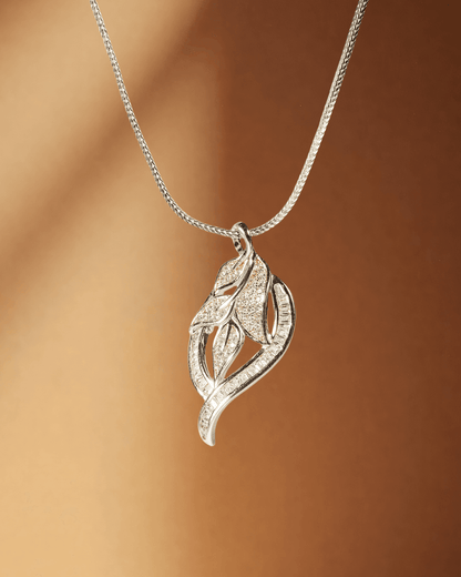 Silver leaf-shaped pendant on a chain against a brown background