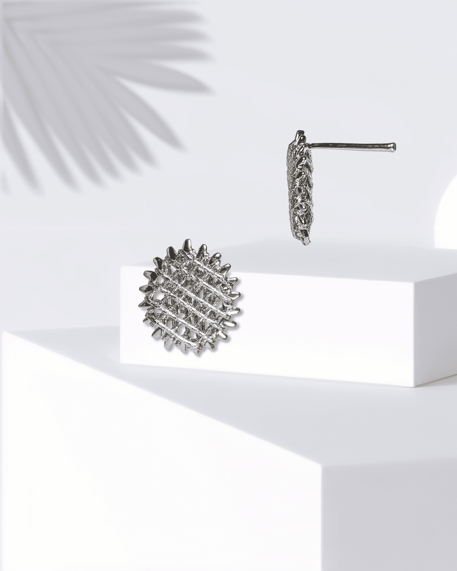 Silver textured earrings on a white surface with a light background