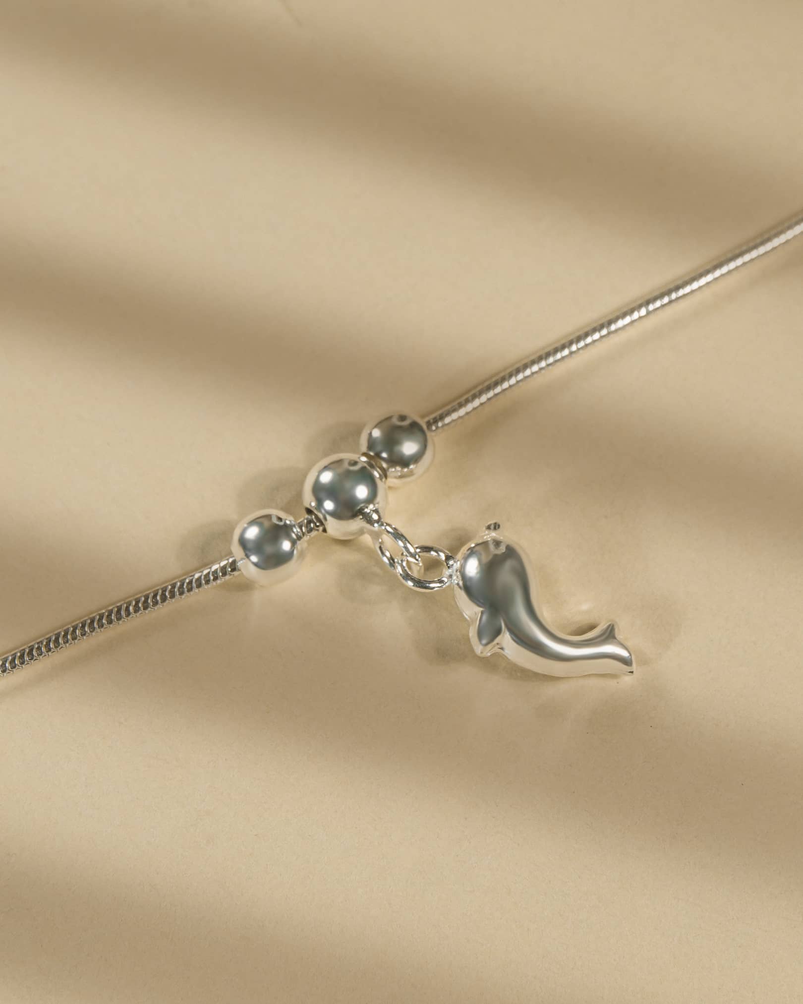 Silver necklace with a dolphin pendant on a beige fabric background