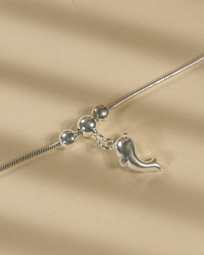 Silver necklace with a dolphin pendant on a beige fabric background