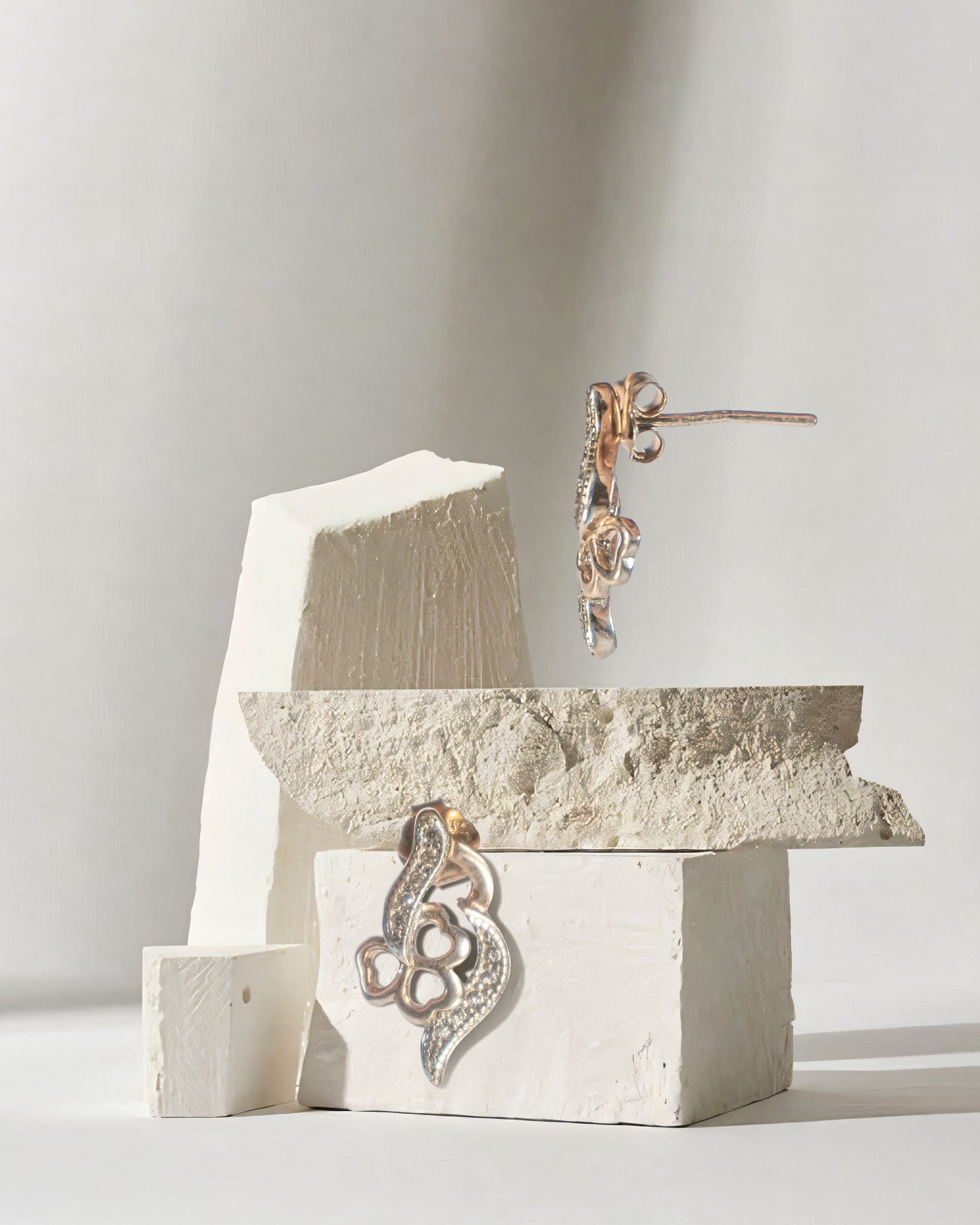 Rose gold earrings on a textured white surface with a neutral background