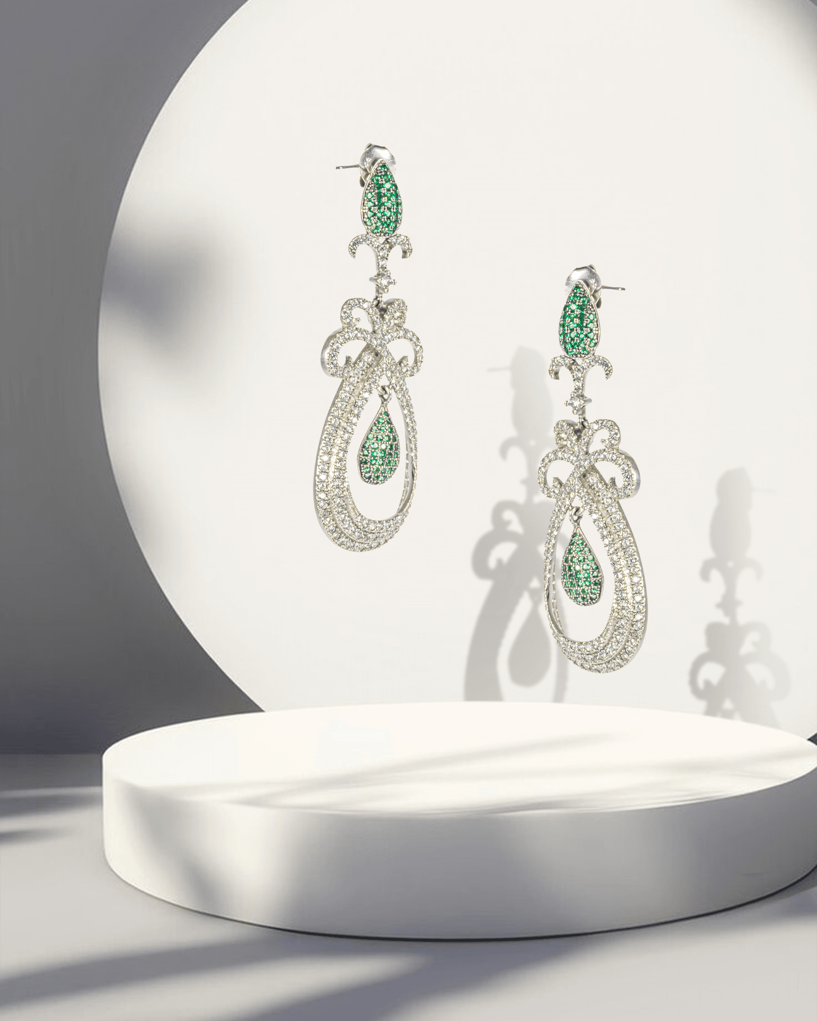 Pair of earrings with green gemstones on a white platform