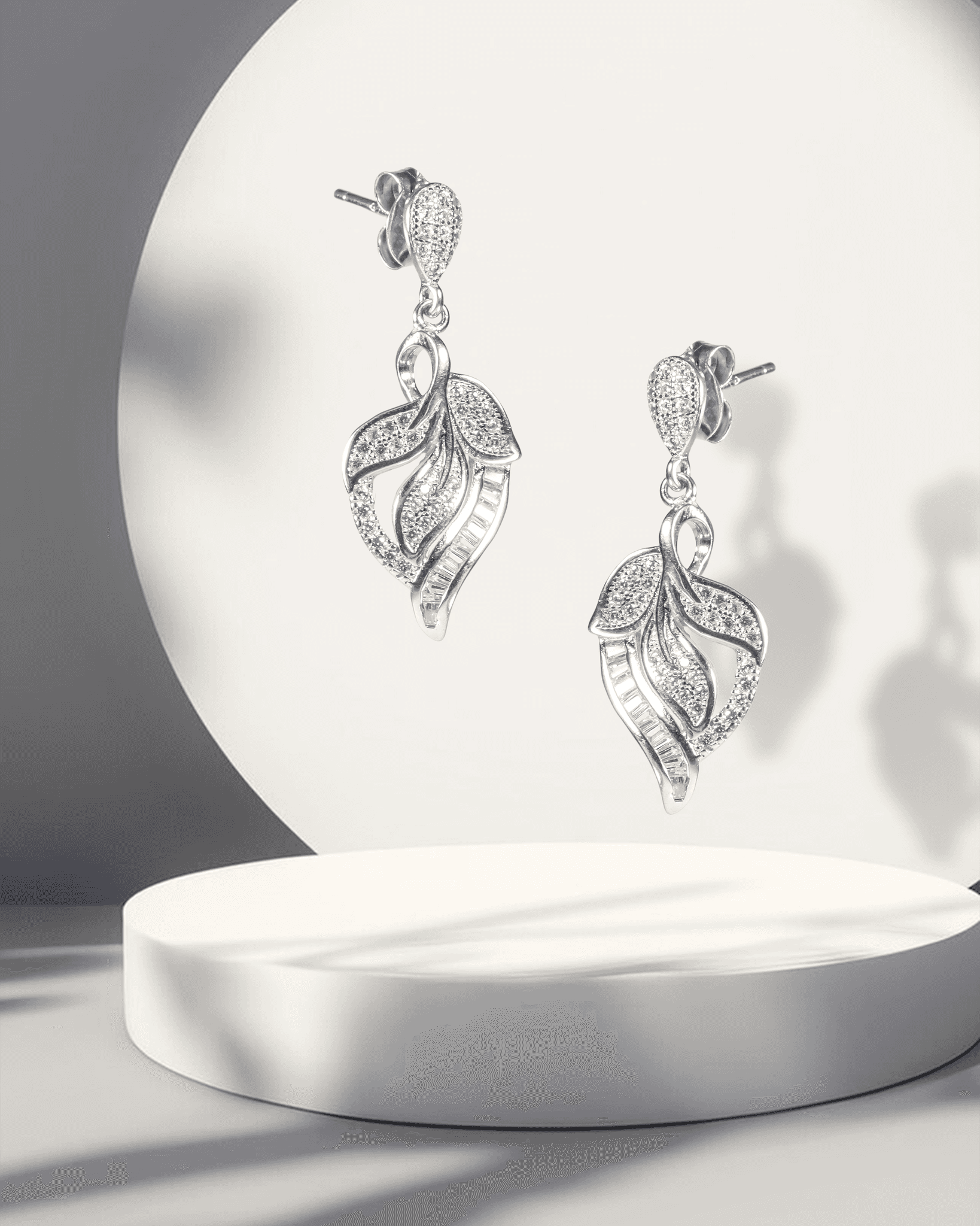 Silver leaf-shaped earrings on a white pedestal with a soft light background