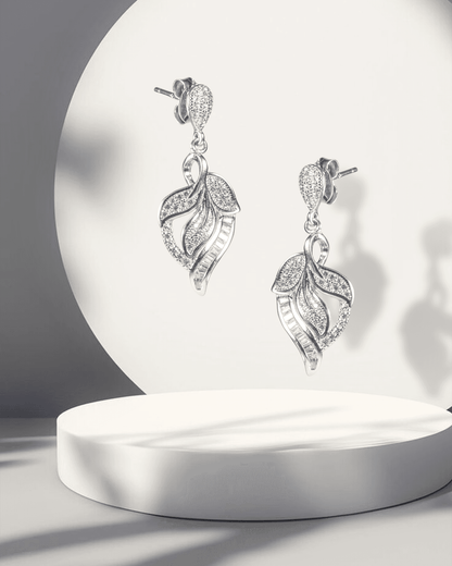 Silver leaf-shaped earrings on a white pedestal with a soft light background