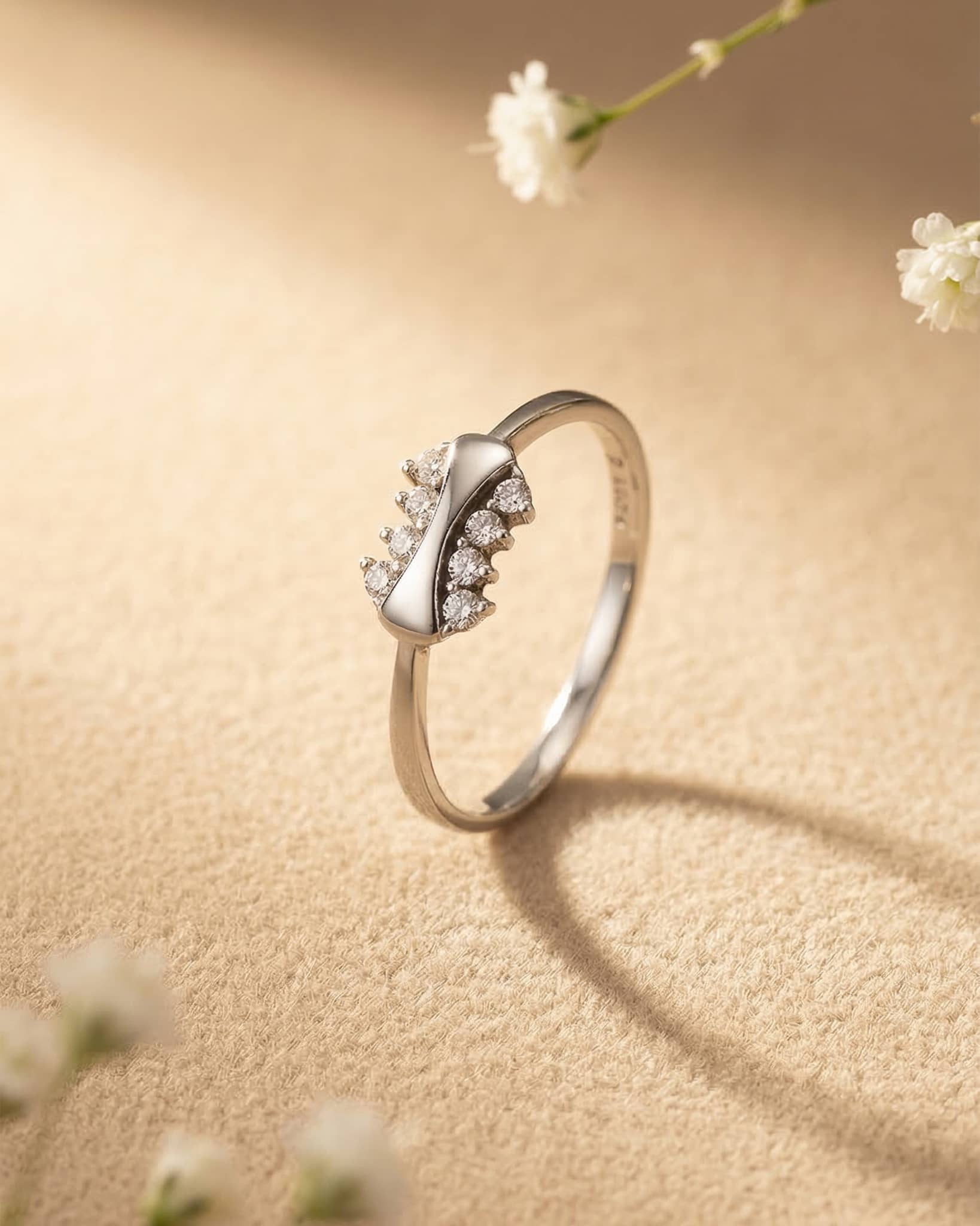 Close up of an elegant silver ring resting on a textured surface, showing a smooth curved ribbon design flanked by brilliant round cz stones.
