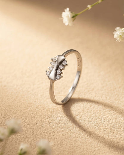 Close up of an elegant silver ring resting on a textured surface, showing a smooth curved ribbon design flanked by brilliant round cz stones.