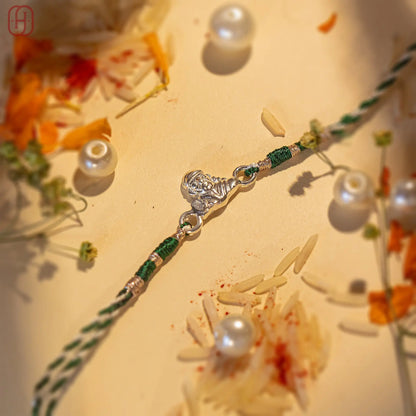 Sai Baba silver rakhi with green and white threads surrounded by flowers and pearls