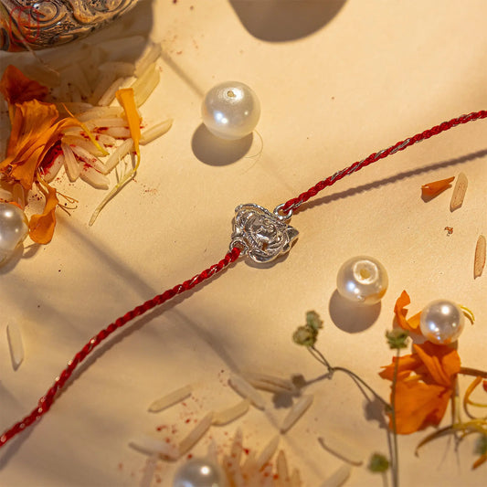 Shiv ji silver rakhi online with red thread and silver Shivji charm decorated with white pearls and marigold petals