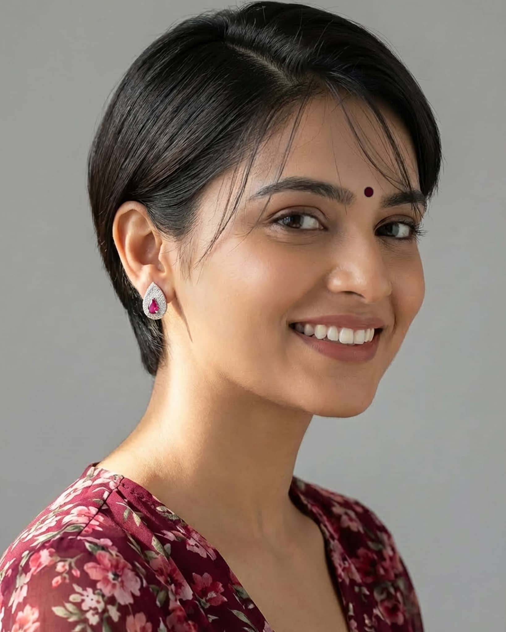 Smiling beautiful woman wearing elegant silver ruby pink cz teardrop pave stud earrings, paired with a maroon floral outfit.
