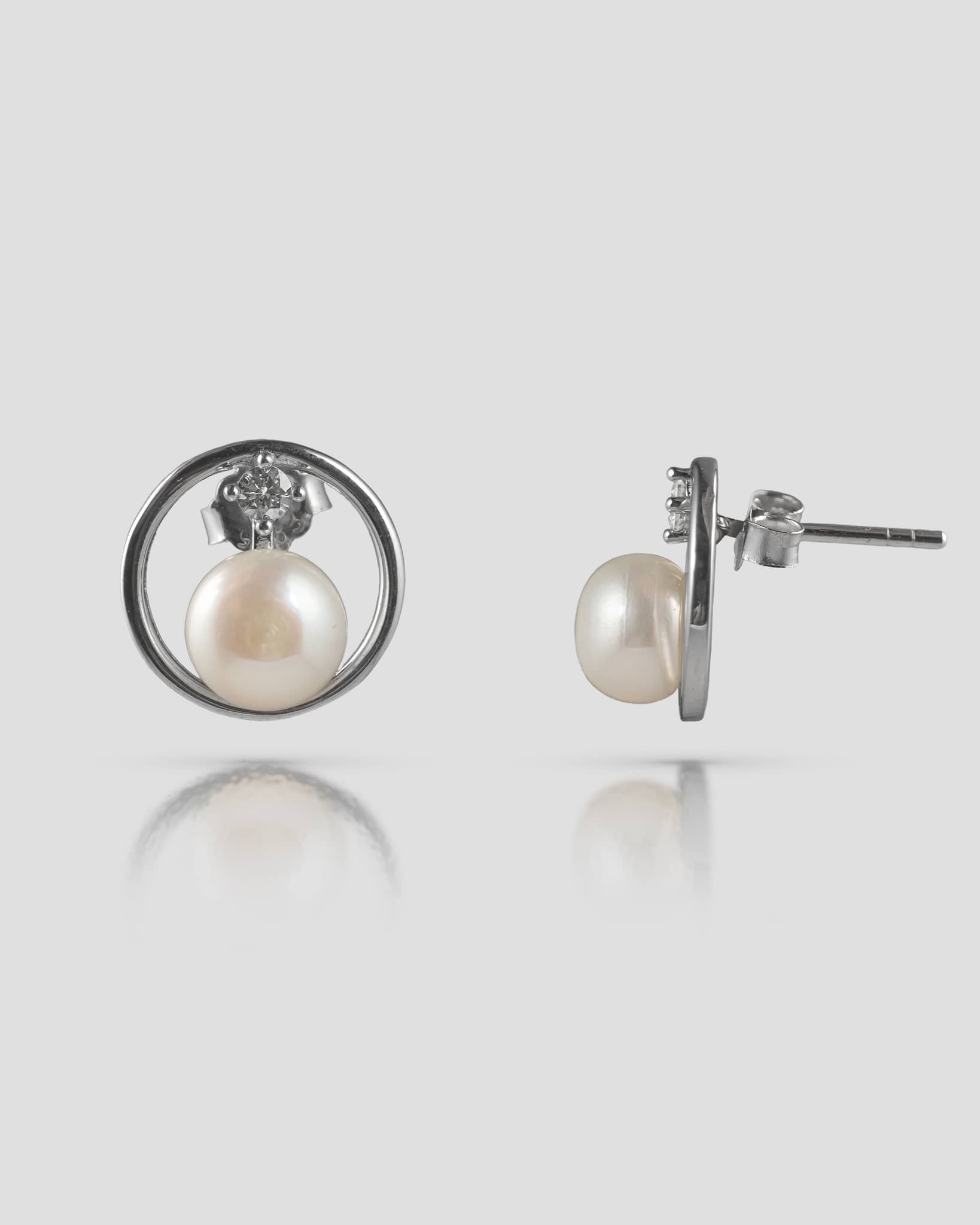 Floating pair of minimalist 92.5 sterling silver open circle stud earrings featuring a white pearl and a delicate clear cz accent.
