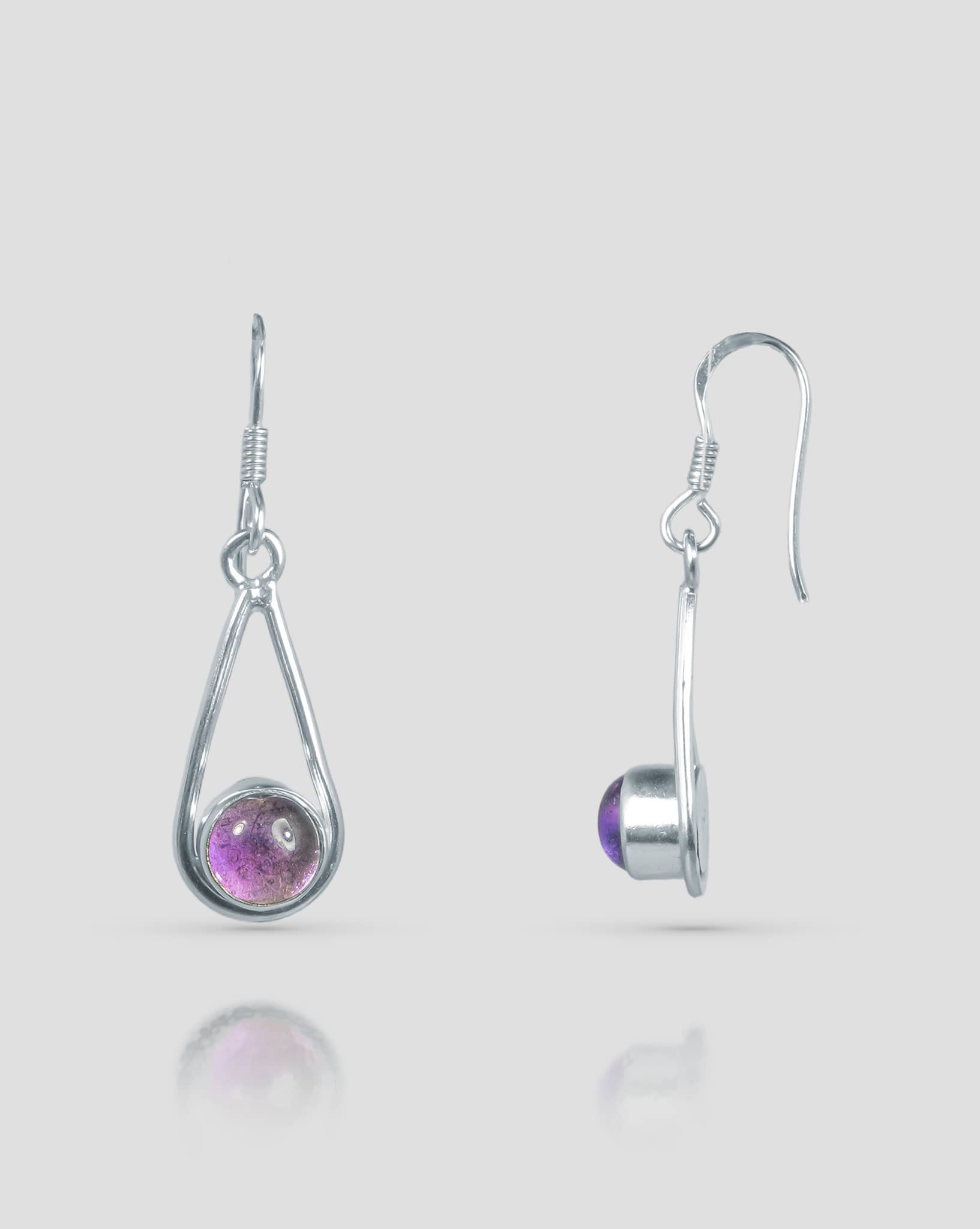 Floating angled shot of minimalist 92.5 sterling silver dangle earrings featuring an open teardrop frame and a smooth round purple cabochon stone at the base.
