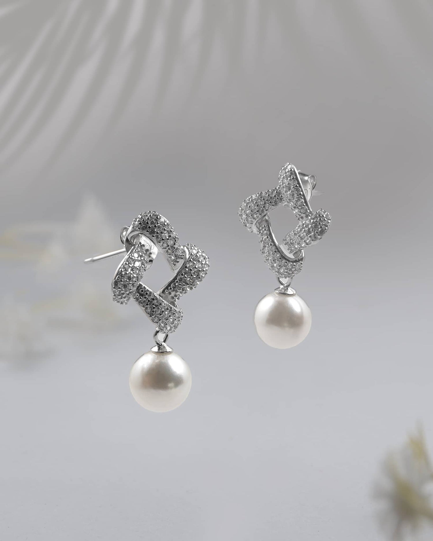 Pair of elegant 92.5 sterling silver dangle earrings featuring a cz paved twisted knot and a round white pearl drop on a textured surface.