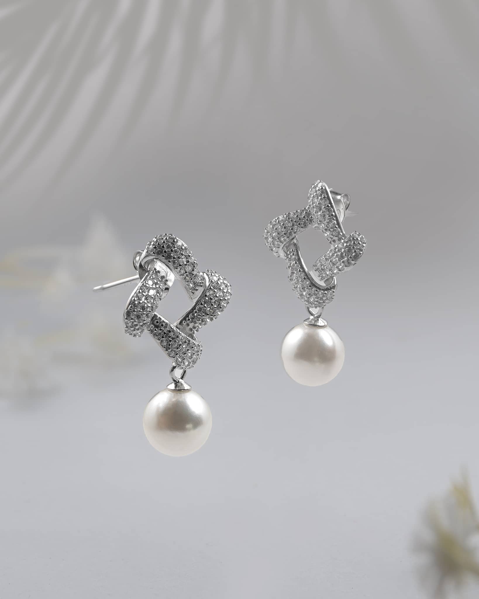 Pair of elegant 92.5 sterling silver dangle earrings featuring a cz paved twisted knot and a round white pearl drop on a textured surface.