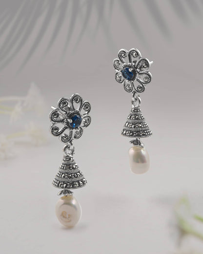 Front and side profile view of silver oxidized floral jhumkis showing the tiered bell, blue center stone, and push-back closure.