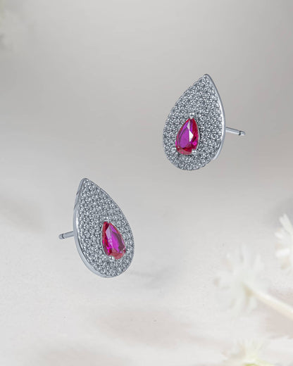 Floating angled shot of 92.5 sterling silver teardrop stud earrings featuring a faceted ruby pink cz center surrounded by a dense clear cz micro-pave halo.