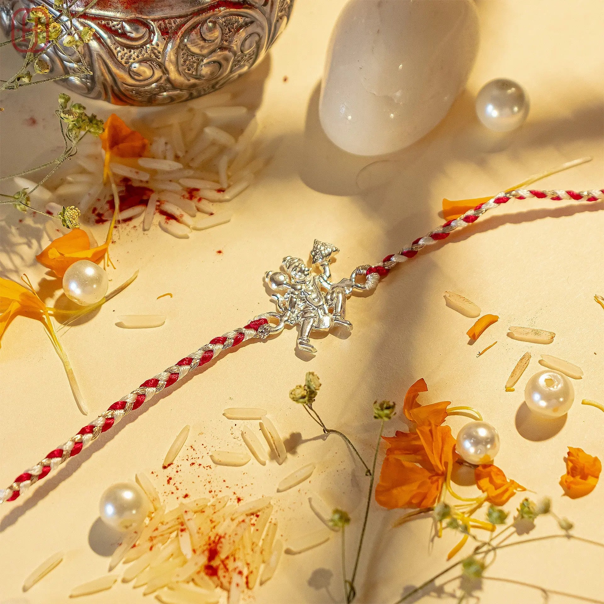 92.5 silver hanuman rakhi with red and white braided thread decorated with flowers, rice, and pearls